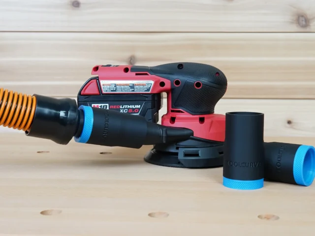Black ToolCurve 1-1/4 inch hose adapter with blue cuff joining an orange hose to a Milwaukee M18 sander, two spare adapters beside it