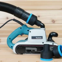 Black ToolCurve 2-1/2 inch hose adapter with blue ring joining a vacuum hose to a Makita 9403 belt sander, spare adapters beside it