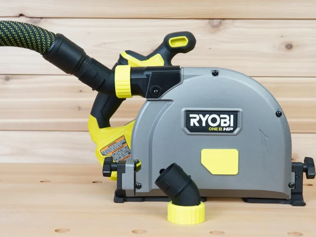 Black and yellow no snag dust port adapter mounted on a Ryobi track saw, with hose attached angled upward from the port