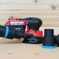 Black 36mm ToolCurve hose adapter with blue trim joining a vac hose to a Milwaukee M18 orbit sander, spare adapters beside it