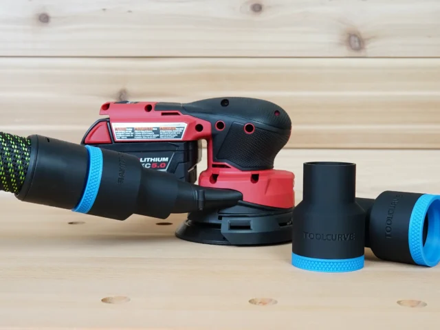 Black 36mm ToolCurve hose adapter with blue trim joining a vac hose to a Milwaukee M18 orbit sander, spare adapters beside it