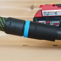 Black hose adapter with blue band attached to Milwaukee Fuel M18 5in Random Orbit Sander dust port, connected to braided hose