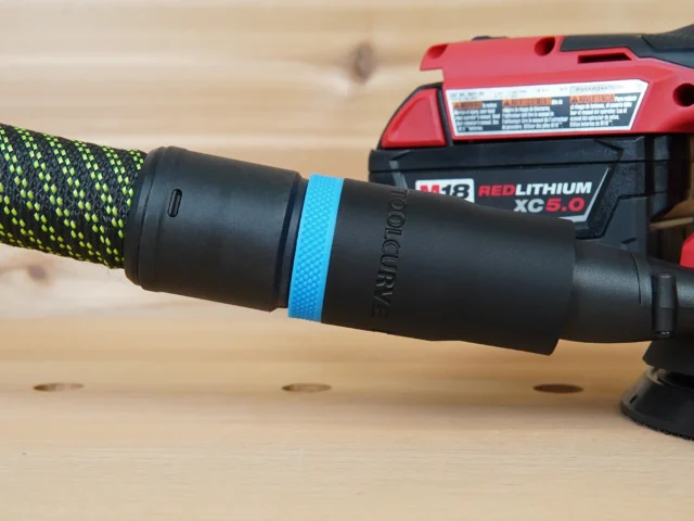 Black hose adapter with blue band attached to Milwaukee Fuel M18 5in Random Orbit Sander dust port, connected to braided hose