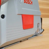 Red snap-on arbor cover attached to gray Bosch track saw, mounted on wood workbench