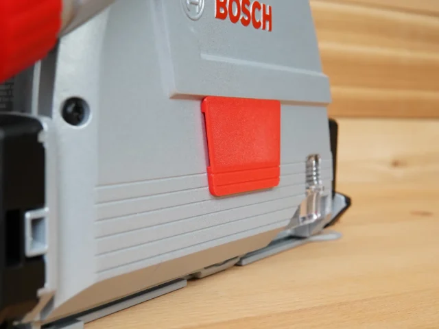 Red snap-on arbor cover attached to gray Bosch track saw, mounted on wood workbench
