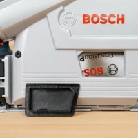 Black arbor cover attached to Bosch GKT13 track saw, shown from below with red dust hose visible above