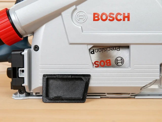 Black arbor cover attached to Bosch GKT13 track saw, shown from below with red dust hose visible above