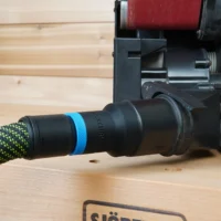 Black hose adapter with blue band attached to green-and-black braided dust hose, mounted on Porter Cable benchtop sander dust port