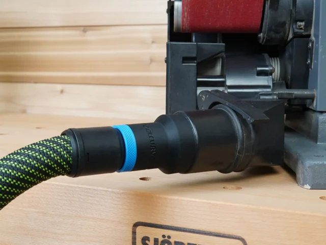 Black hose adapter with blue band attached to green-and-black braided dust hose, mounted on Porter Cable benchtop sander dust port
