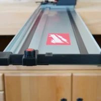 Black hose deflector with red knob mounted on Milwaukee guide rail with ToolCurve branding visible on rail surface