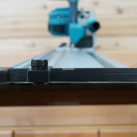 Black hose deflector with clamping knob mounted on Makita track saw guide rail, side view showing deflector wings and adjustment knob