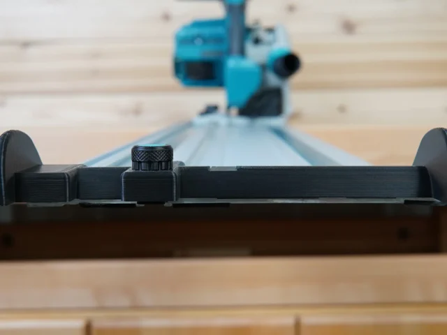 Black hose deflector with clamping knob mounted on Makita track saw guide rail, side view showing deflector wings and adjustment knob