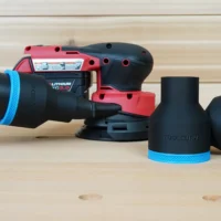 Black 2-1/2 inch hose adapter with blue trim connected to a vacuum hose beside a Milwaukee M18 sander and two spare adapters
