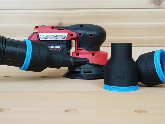 Black 2-1/2 inch hose adapter with blue trim connected to a vacuum hose beside a Milwaukee M18 sander and two spare adapters