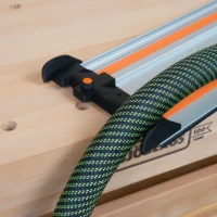 Black hose deflector mounted on a Wen track saw rail, with an orange quick-release clamping knob and green braided hose routed through the deflector