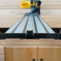 Black hose deflector mounted on Dewalt track saw guide rails, front view showing clamping knob and side handles