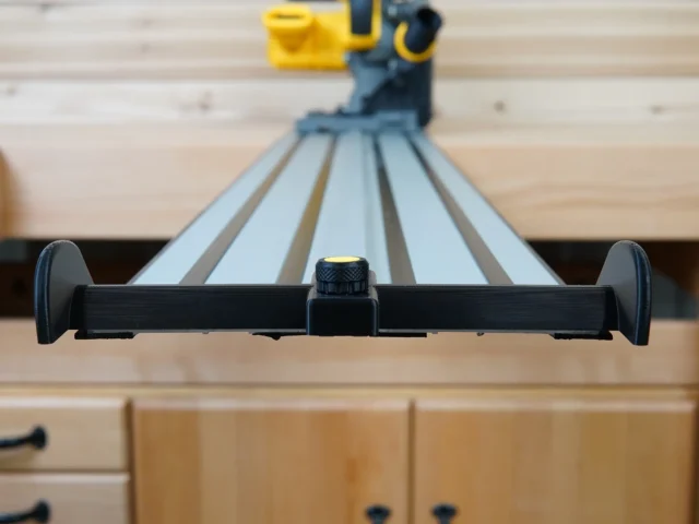 Black hose deflector mounted on Dewalt track saw guide rails, front view showing clamping knob and side handles