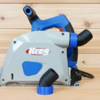 No Snag Dust Port for Kreg track saw shown attached to a Kreg track saw, with blue and black hose adapter angled upward away from the tool base