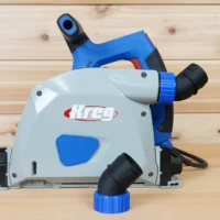 No Snag dust port with blue threaded collar installed on a Kreg track saw, angling the hose port upward, plus a second adapter shown beside it