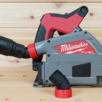 No Snag Dust Port attached to a Milwaukee track saw with black and green hose inserted, showing the angled port directing hose upward and away from the tool