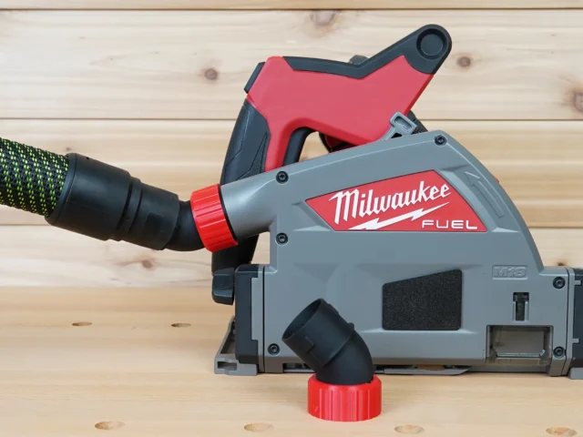 No Snag Dust Port attached to a Milwaukee track saw with black and green hose inserted, showing the angled port directing hose upward and away from the tool