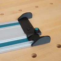 Black hose deflector with teal clamping knob mounted across the end of a Makita guide rail on a workbench