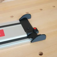 Black hose deflector with red clamping knob mounted across the end of a Milwaukee guide rail on a workbench
