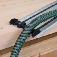Black hose deflector mounted on Milwaukee guide rail with green braided hose routed through it, installed on track saw