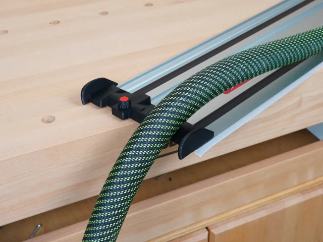 Black hose deflector mounted on Milwaukee guide rail with green braided hose routed through it, installed on track saw