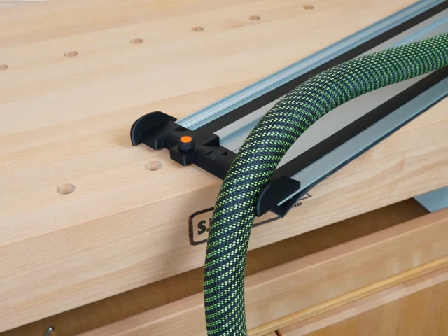 Black hose deflector mounted on a Powertec track saw guide rail, with green braided hose routed through it and an orange adjustment knob visible