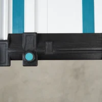 Black 3D-printed hose deflector with turquoise clamping knob, mounted on Makita guide rail with white and turquoise channels