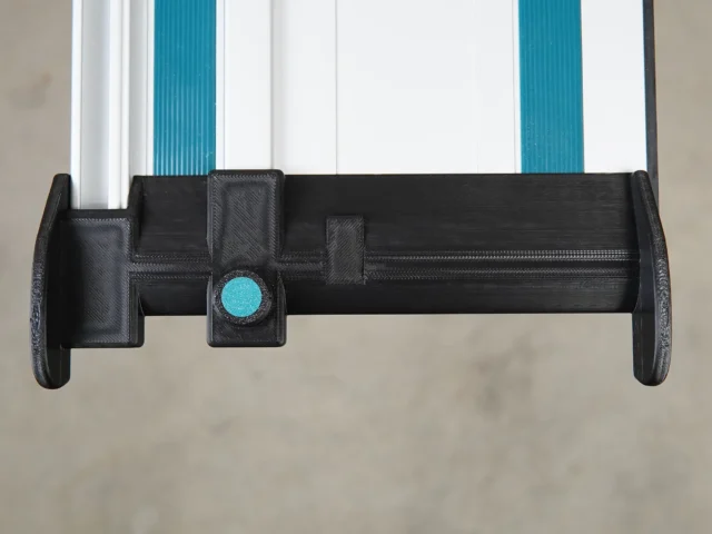 Black 3D-printed hose deflector with turquoise clamping knob, mounted on Makita guide rail with white and turquoise channels