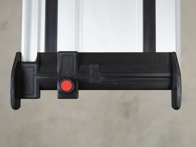 Black 3D-printed hose deflector mounted on Milwaukee track saw guide rails with red quick-release clamping knob, front view