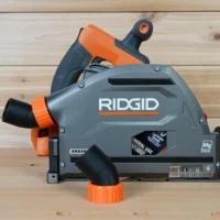 ToolCurve no snag dust port adapter mounted on a Ridgid track saw, gray and orange, with hose angled upward away from the tool