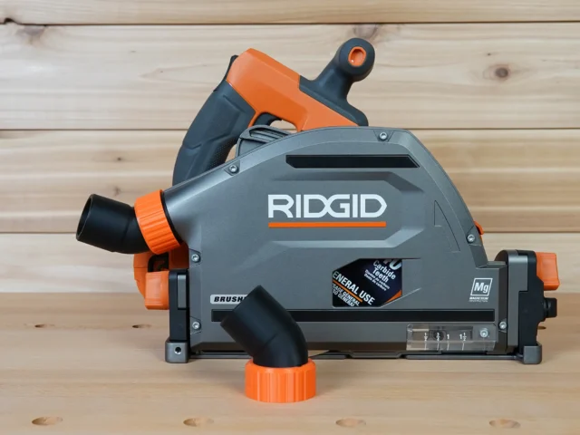 ToolCurve no snag dust port adapter mounted on a Ridgid track saw, gray and orange, with hose angled upward away from the tool