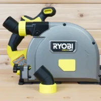 No snag dust port adapter for Ryobi track saw mounted on saw body, with yellow hose collar and black angled port directing hose away from deck