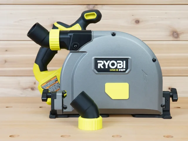 No snag dust port adapter for Ryobi track saw mounted on saw body, with yellow hose collar and black angled port directing hose away from deck