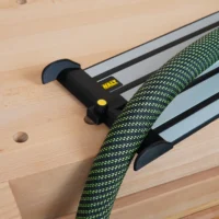 Black hose deflector with yellow knob mounted on a DeWalt guide rail, with green fabric hose routed through the deflector