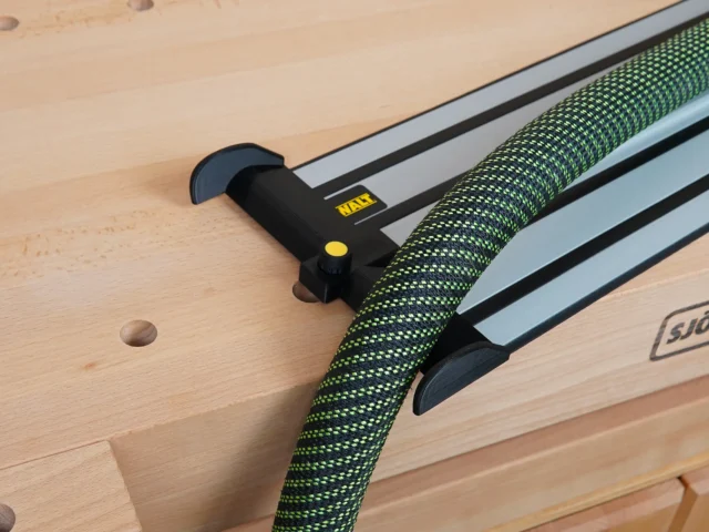Black hose deflector with yellow knob mounted on a DeWalt guide rail, with green fabric hose routed through the deflector