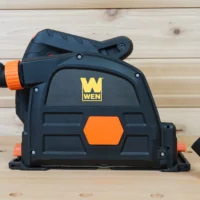 Wen track saw dust port with orange hose connector and removable port cap, shown from front angled view next to detached cap on wooden surface