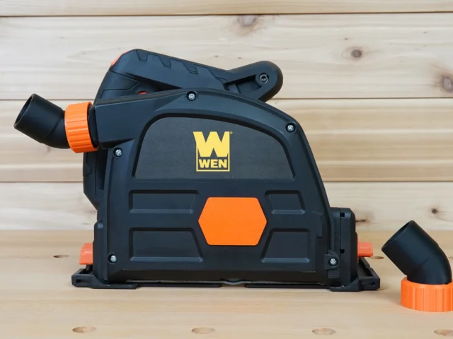 Wen track saw dust port with orange hose connector and removable port cap, shown from front angled view next to detached cap on wooden surface