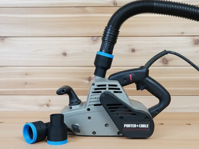 Black 1-7/8 inch hose adapter with blue band joining a vacuum hose to a Porter Cable belt sander, spare adapter beside it