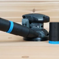 Black ToolCurve hose adapter with blue ribbed collar standing beside a Flex random orbital sander and vacuum hose