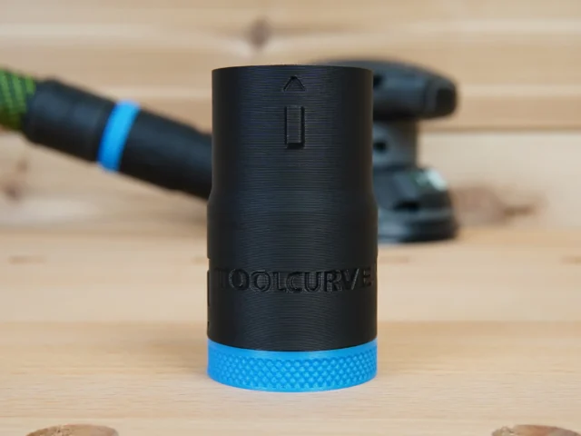 Black ToolCurve hose adapter with blue band, shown standalone on wood with a Flex sander and hose in the background