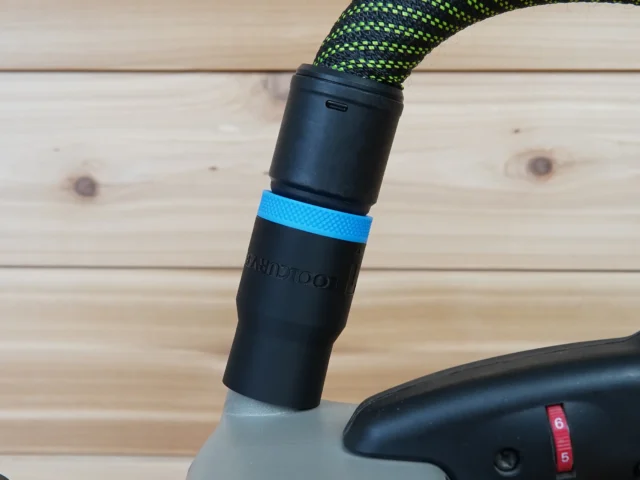 Black hose adapter with blue band attached to Porter Cable belt sander dust port, with green and black braided hose connected above