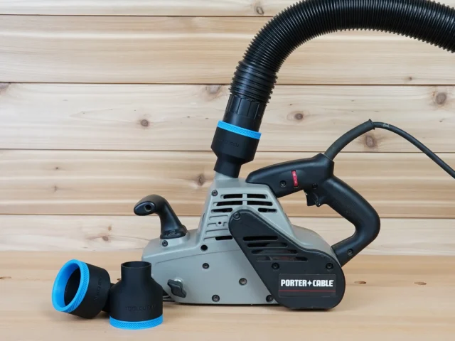 Black 2-1/2 inch hose adapter with blue trim installed on a Porter Cable belt sander, two spare adapters beside it