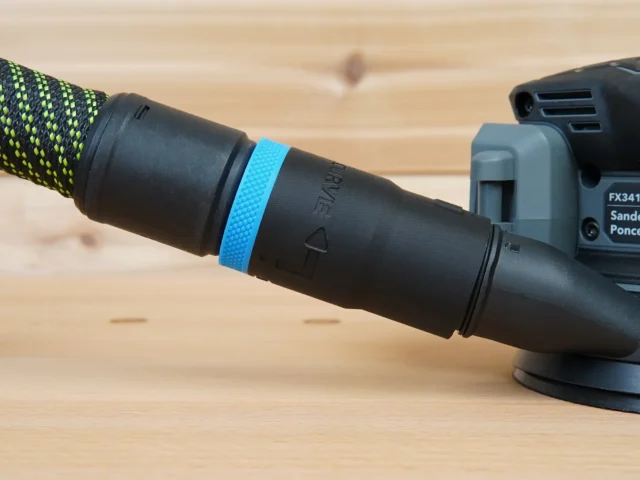 Black hose adapter with blue identification band attached to a Flex sander's dust port, connected to a green-and-black braided hose