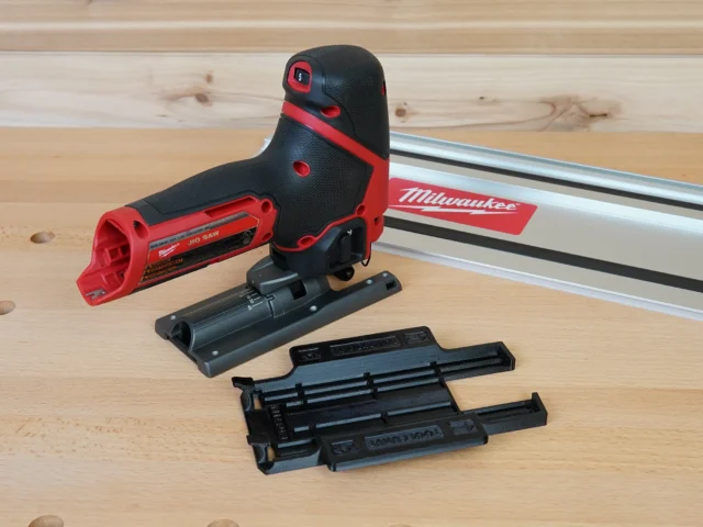 Milwaukee M12 Fuel jig saw with red and black adapter mounted on base, shown disassembled with track rail connector and replacement base plate on wooden workbench