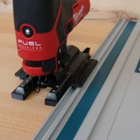 Milwaukee M12 Fuel jig saw mounted on a track saw guide rail via black plastic adapter with dual contact feet