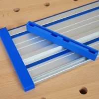 Blue PETG protective caps fitted over both ends of a Kreg ACS aluminum guide rail on a wood workbench